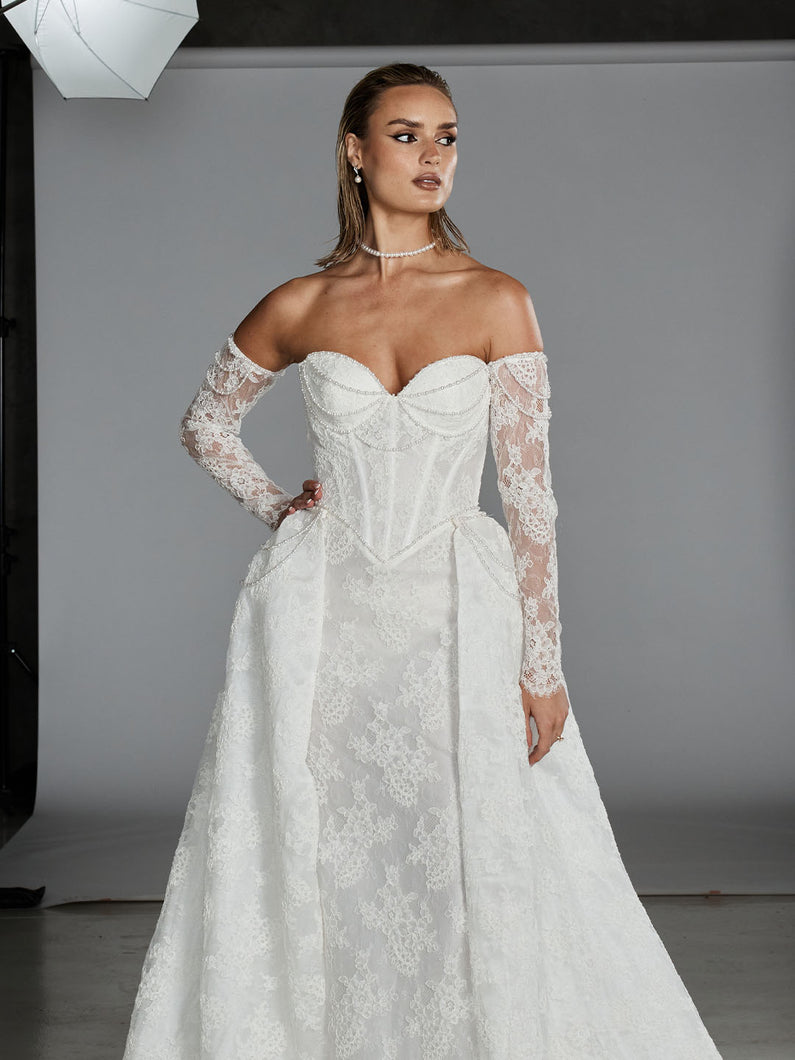 Bardot by Evie Young – strapless lace fit-and-flare wedding dress with detachable overskirt and pearl draping.